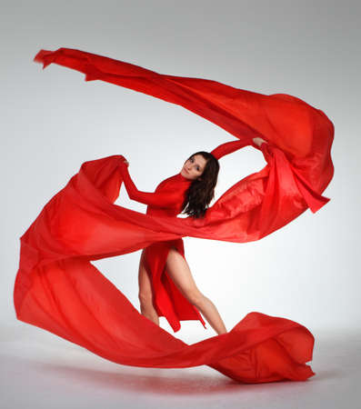 Young brunette woman dancing with red fabric in studioの写真素材
