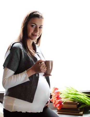 Happy smiling pregnant woman drinking tea near the windowの写真素材