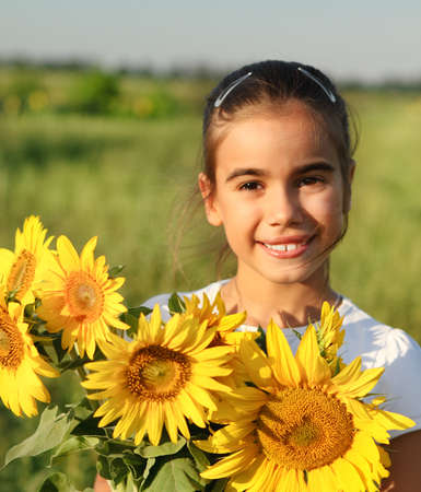 Cute little smiling child with sunflowers in summer field. Sunsetの写真素材