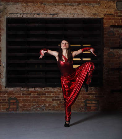 Young brunette woman in red dancing over brick wallの写真素材