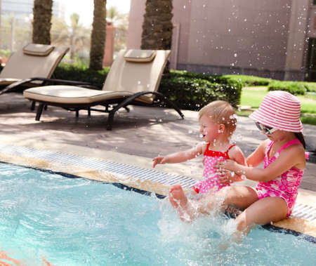 Two little sisters playing in water in swimming poolの写真素材