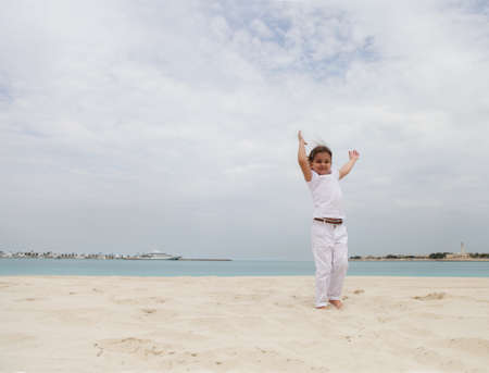 Little happy girl in white jumping on the beachの写真素材