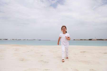 Little happy girl in white jumping on the beachの写真素材