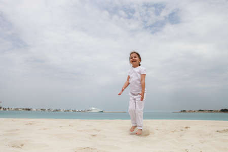Little happy girl in white jumping on the beachの写真素材