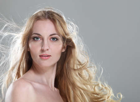 Young woman with blond fluttering hair over gray backgroundの写真素材