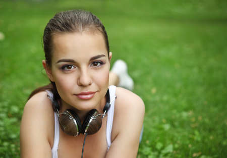 Beautiful young girl with headphones lying on the grass in summer parkの写真素材