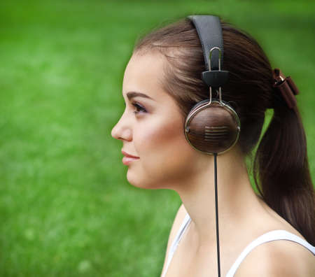 Beautiful young girl with headphones on the grass background in summer parkの写真素材