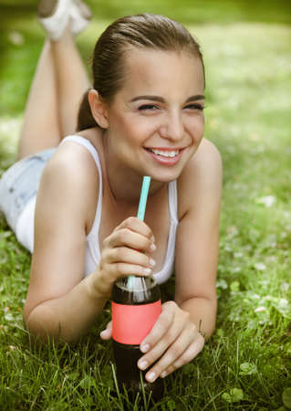 Beautiful young drinking girl lying on the grass in summer parkの写真素材