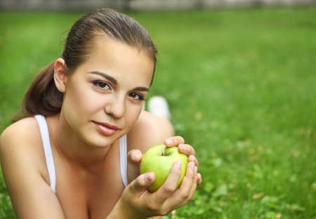 Beautiful young girl with green apple lying on the grass in summer parkの写真素材