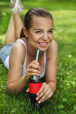 Beautiful young drinking girl lying on the grass in summer parkの写真素材