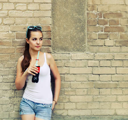 Beautiful young girl with drink near the brick wallの写真素材