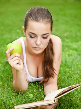 
Beautiful young girl lying on the grass and reading in summer parkの写真素材