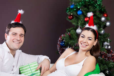 Happy pregnant couple with presents near the christmas tree の写真素材