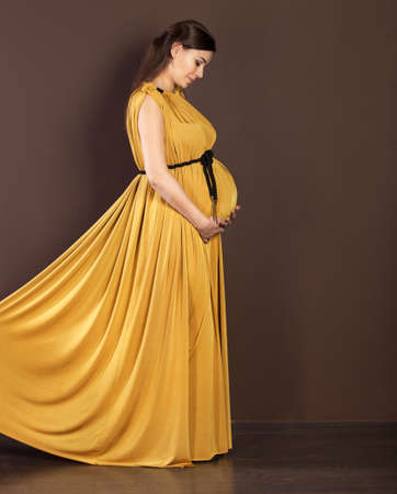 Happy pregnant woman in beautiful long dress touching her bellyの写真素材