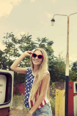 Blond girl holds hands on her glasses standing on damaged gas stationの写真素材