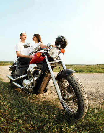 Young biker couple on the country road against the sky