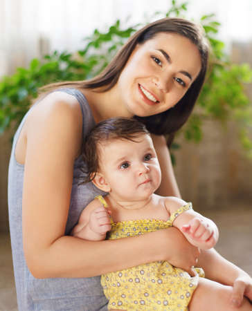 Happy smiling mother with eight month old baby girl indoorの写真素材