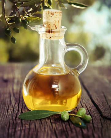 Olive oil and olive branch on the wooden table over nature backgroundの写真素材