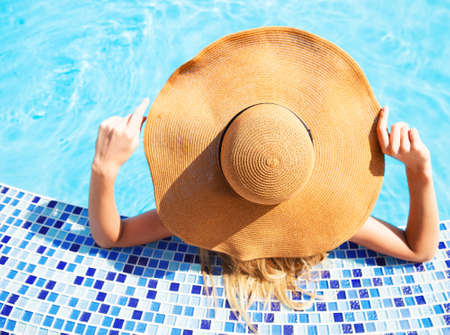 Pretty woman in a hat enjoying a swimming pool