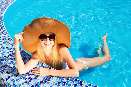 Pretty blond woman in a hat enjoying a swimming poolの写真素材