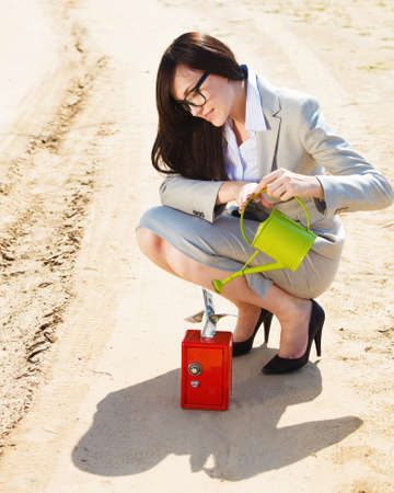 Businesswoman watering a money in safe in a desert. Conceptの写真素材
