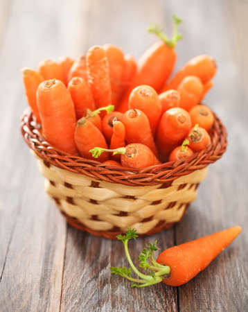 Fresh organic carrots in small basket on a wooden tableの写真素材