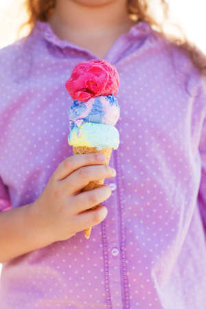 Little smilling girl holding ice cream cone in her hands outdoorsの写真素材
