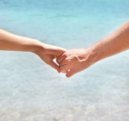 Young couple in love holding hands. Summer sea background. Close upの写真素材