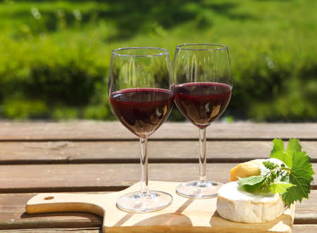Various sorts of cheese, grape leaves and two glasses of the natural homemade red wineの写真素材