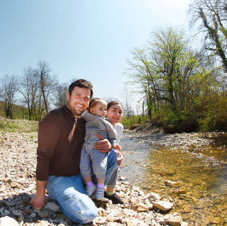 Happy young family with little daughter near the mountain river outdoorsの写真素材