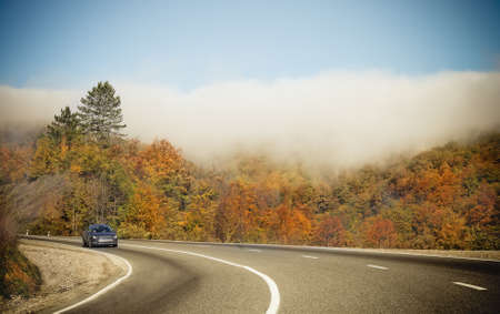 Foggy autumnal mountain road with lonely car