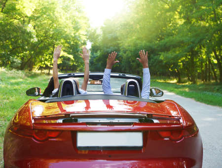 Happy free couple driving in red retro car cheering joyful with arms raised. Road trip travel conceptの写真素材