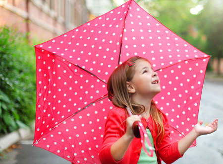Child with polka dots umbrella wearing red rain boots jumping into a puddleの写真素材
