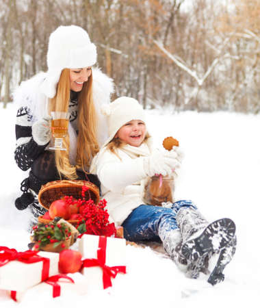 Happy young mother with daughter with hot tea and cookies and christmas decorations on winter picnicの写真素材