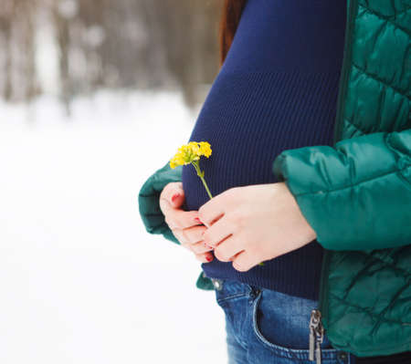 Young beautiful pregnant woman in winter clothes outdoorsの写真素材