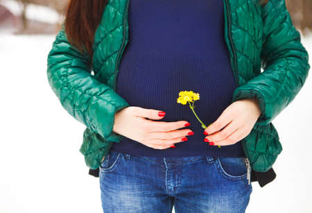 Young beautiful pregnant woman in winter clothes outdoorsの写真素材