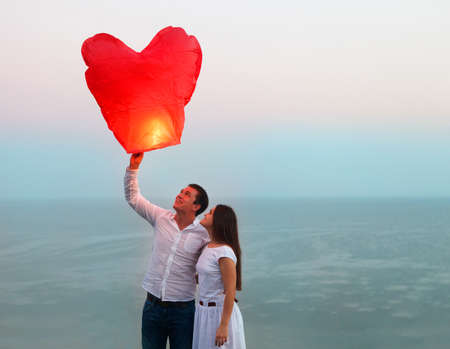 Young couple start a red Chinese sky lantern in the dusk near the seaの写真素材