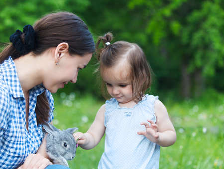 Cute little girl and her mother hugging little grey rabbitの写真素材