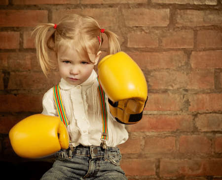 Little girl with yellow boxing gloves over brick wall backgroundの写真素材