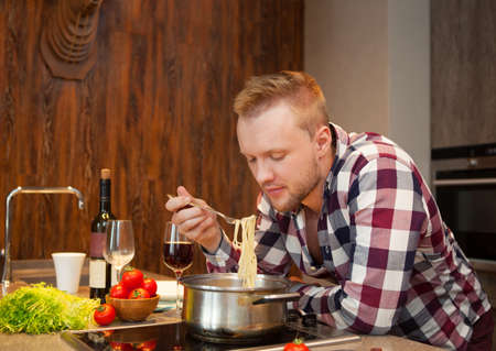 Handsome man cooking at home preparing pasta in a kitchenの写真素材