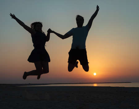 Silhouette of a couple - man and woman jumping on the beach at sunset の写真素材