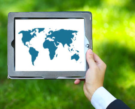 Man holding tablet computer with world map on the green grass backgroundの写真素材