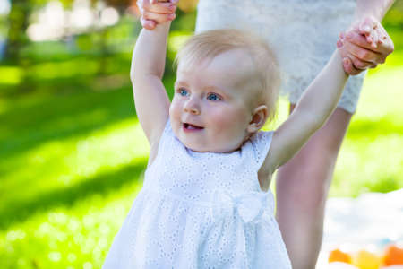 Baby learning to walk outdoors. Happy mum and her Child playing in Park together. Outdoor Portrait...