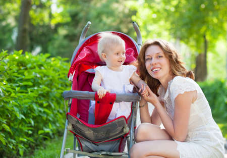  Beautiful young woman with her child in a baby carriage in the parkの写真素材