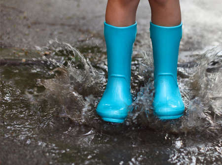 Child wearing blue rain boots jumping into a puddle. Close up