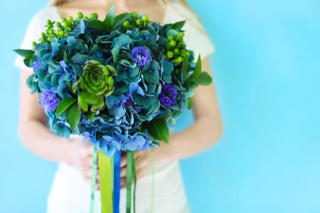 A wedding bouquet with hydrangea in blue and green colors outdoors in hands of a brideの写真素材
