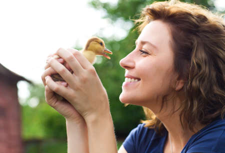 Young caucasian woman with yellow duckling outdoors at green nature backgroundの写真素材