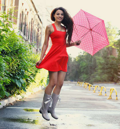 Portrait of beautiful young girl jumping with umbrella under rainの写真素材