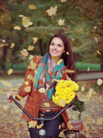 Beautiful happy woman with bike in autumn parkの写真素材