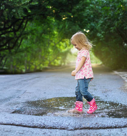 Cute little girl wearing rain boots jumping into a puddleの写真素材